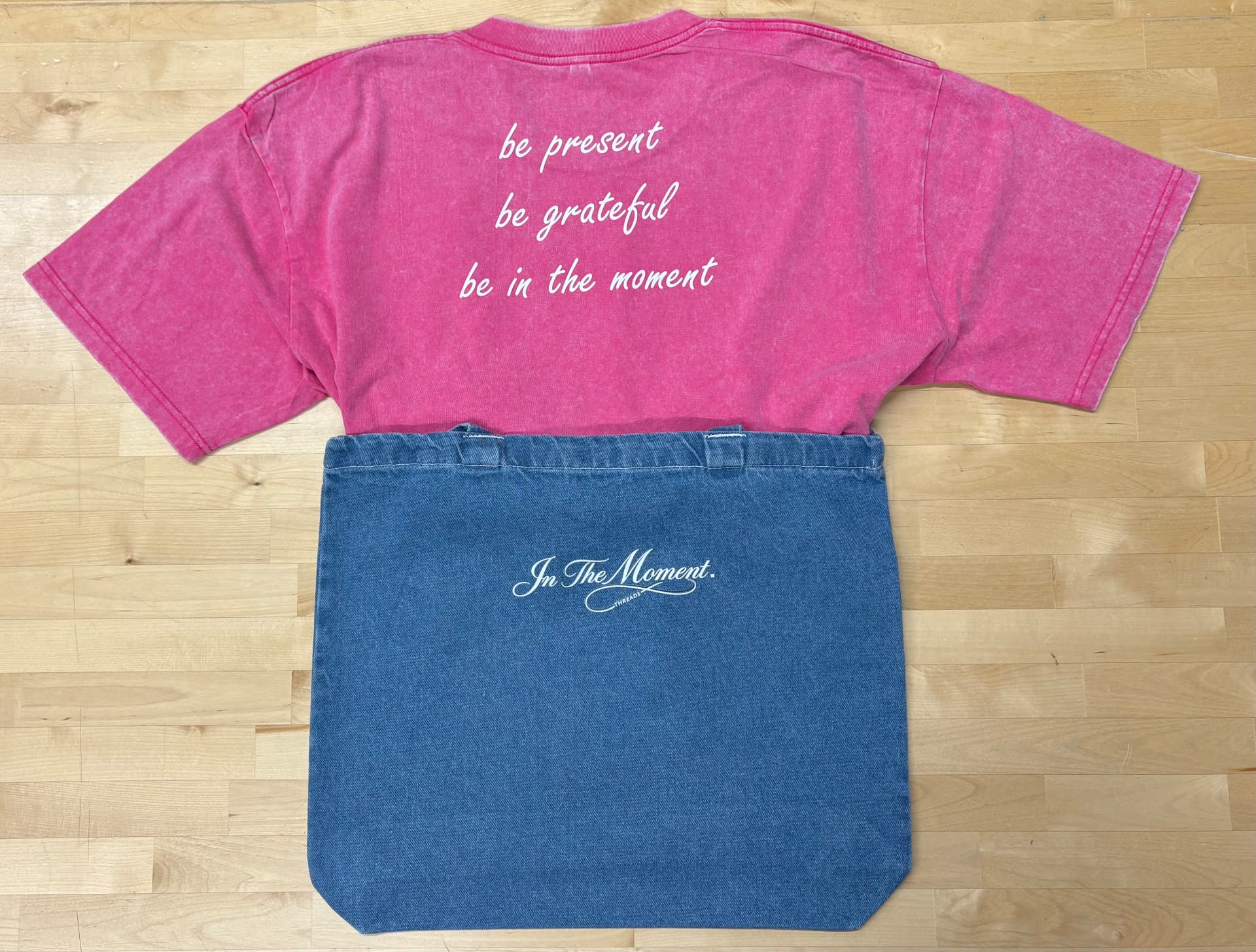 Pink In The Moment tee back with be present message next to a denim tote